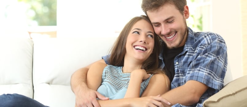 Hombres y mujeres felices y amorosos sonriendo y sentados en el sofá de la sala de estar