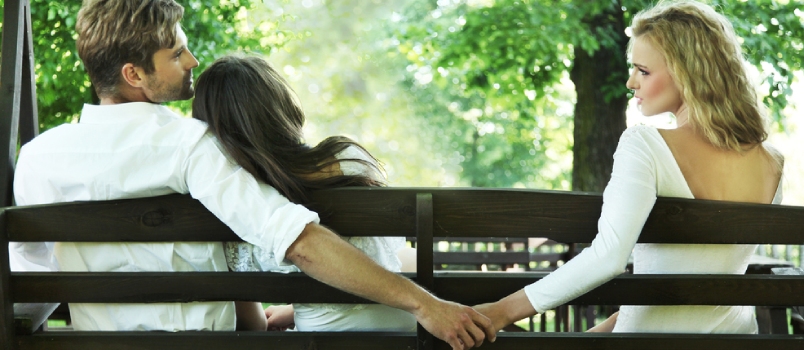 Hombre casado sosteniendo la mano de otra mujer mientras todos se sientan en un banco del parque