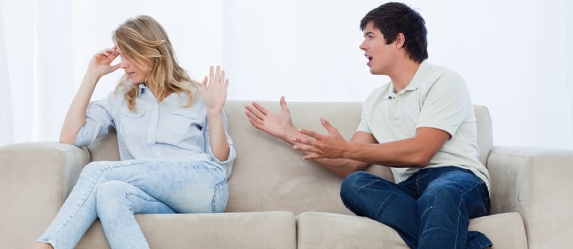 Un hombre sentado en un sofá discute con su novia que tiene la cabeza vuelta hacia otro lado