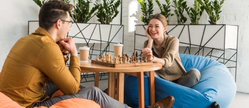 Jóvenes amigos felices jugando al ajedrez mientras están sentados en pufs