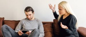 Hombre con smartphone en mano mientras su esposa lo intimida verbalmente