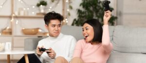 Pareja joven coreana jugando videojuegos juntos, marido asiático perdiendo videojuego con esposa sentada en la sala de estar de casa
