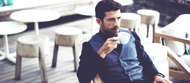 Un hombre de negocios exitoso y confiado en traje disfrutando de una taza de café mientras almuerza en un restaurante moderno