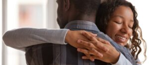 Atractiva y amorosa novia afroamericana abraza a su novio, de pie en casa con los ojos cerrados
