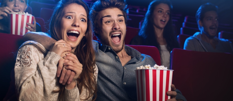 Una joven pareja asustada en el cine viendo una película de terror y gritando, ella sostiene la mano de su novio