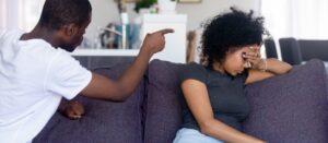 Hombre afroamericano enojado peleando, gritando emocionalmente a una mujer molesta, sentada en el sofá en casa