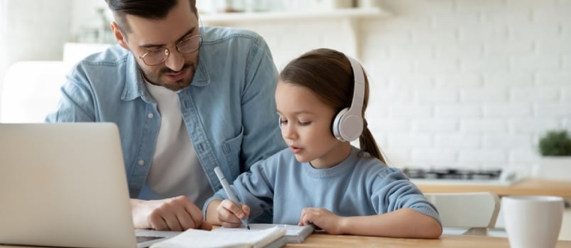 Un padre joven y cariñoso ayuda a su pequeña hija en edad preescolar a estudiar juntas y ver una lección en línea en una computadora portátil