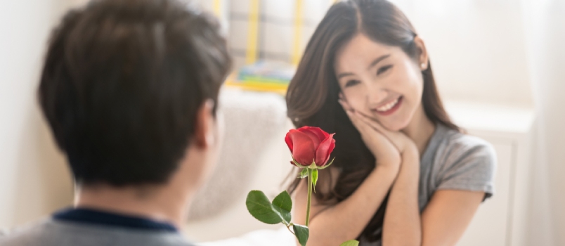 Joven asiático dando flor rosa roja a una mujer bonita.  Chica recibiendo un encantador regalo de San Valentín sintiendo amor y tímida sonrisa en la cara